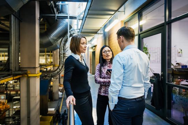 two women and a man standing in a hallway and talking